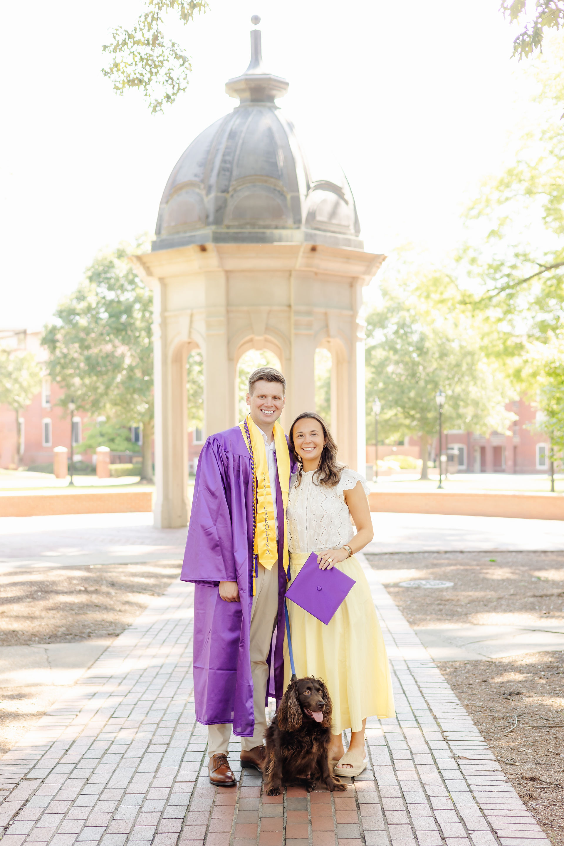 ECU graduates posing with dog in front of East Carolina University Cupola.