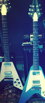 Two Flying V guitars on stands in front of a Marshall stack in the War Gods of the Deep studio