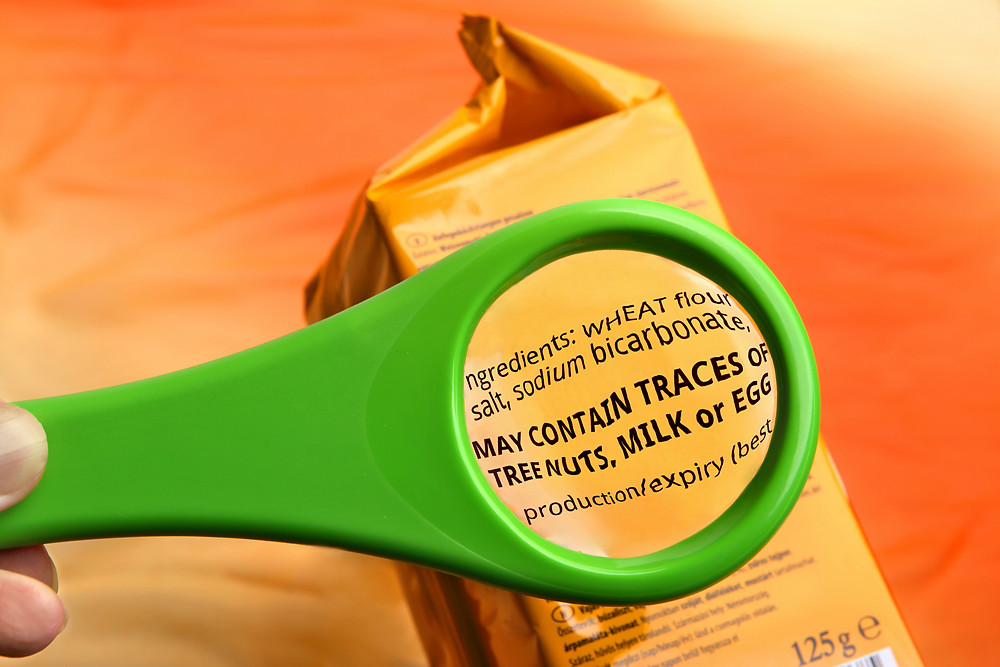 Green Magnify glass looking at a brown bag with the words enlarged May contain traces of tree nuts, mils or egg