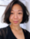 The artist who self-identifies as queer Chinese American born cis-gender female with chin-length hair wears a black top is smiling while standing in front of a white marbled wall.