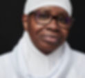 This is a professional head shot of an African American women in all white Islamic attire, wearing brown eye glasses that shape and contrast her brown eyes, and a slit smile can be seen, although her mouth is closed through the arch in her cheek bones.