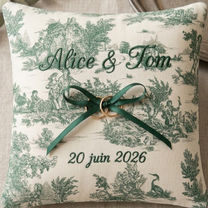 un coussin d'alliances en toile de jouy, délicatement brodé avec les prénoms et la date de mariage. Un lien en satin est cousu au milieu du coussin, pour attacher les alliances avec un noeud