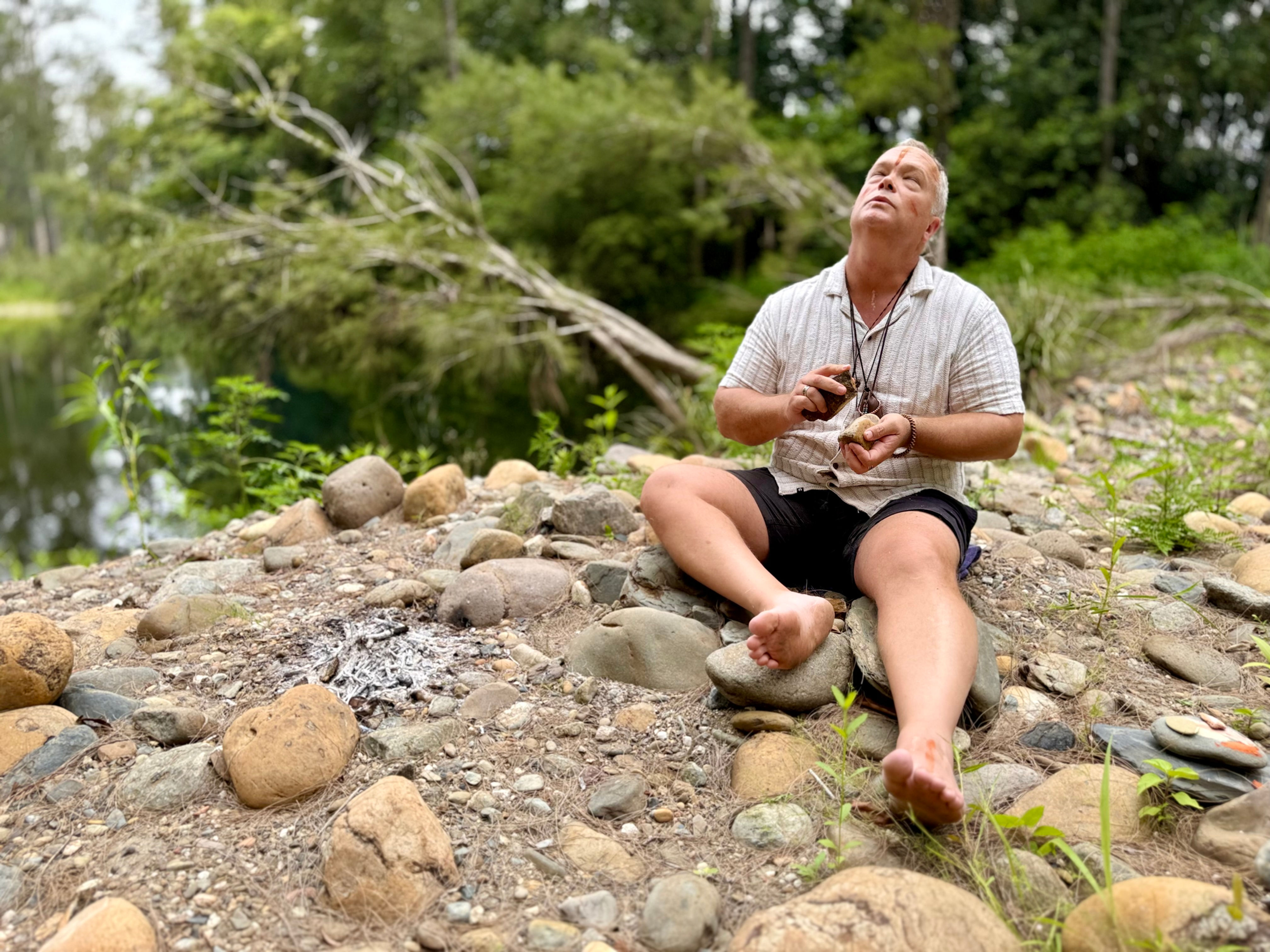 Man sitting barefoot by river, looking up