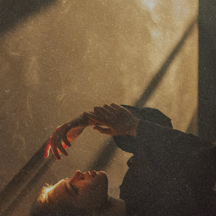 A warm, grainy photo of a hand reaching toward a rain-streaked window in soft golden light.
