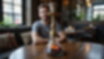 A man in a gray shirt sits at a wooden table with a lit hookah. Cozy cafe setting, cushioned seats, and candlelit tables in the background.