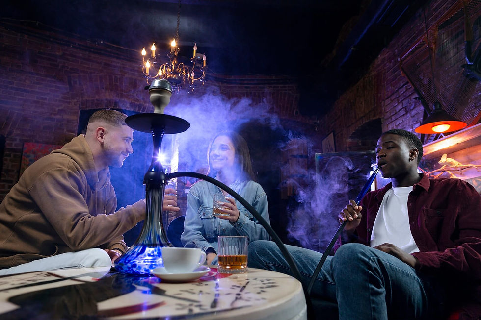 Three people enjoying hookah in a dimly lit lounge with a brick wall. Blue hookah, drinks on the table, relaxed atmosphere.