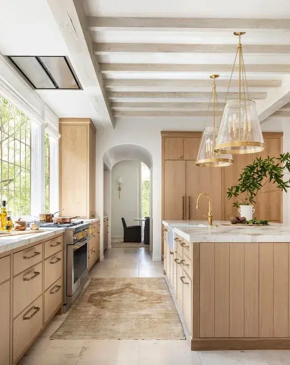 Glass lantern pendant lights in brass finish over the kitchen island, complementing the wood cabinets and marble countertops.