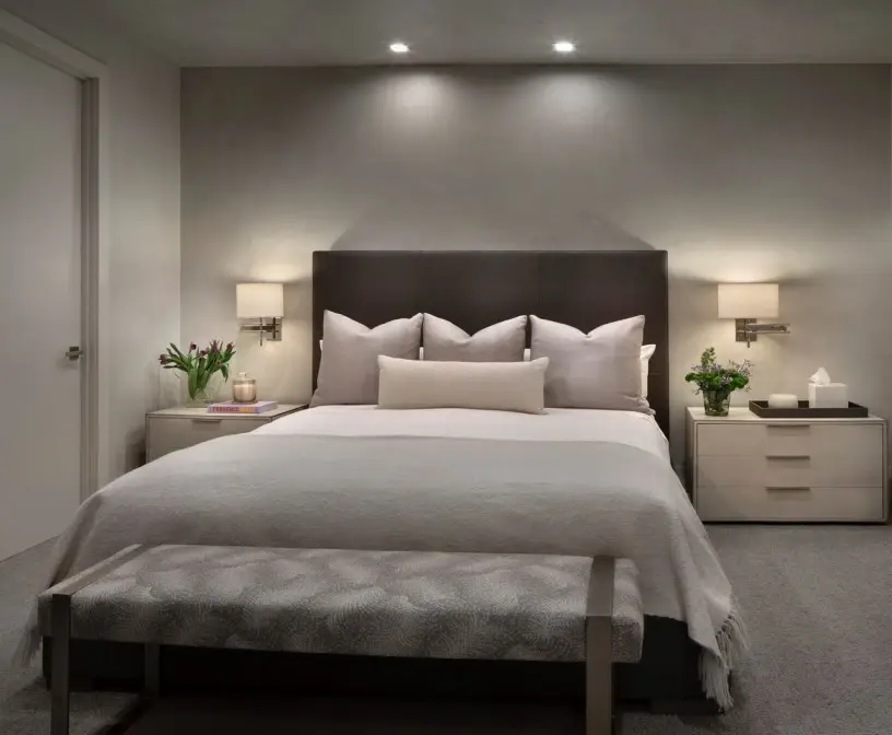 Layered lighting in the bedroom with recessed ceiling lights and wall sconces, creating a soft, ambient glow around the area.