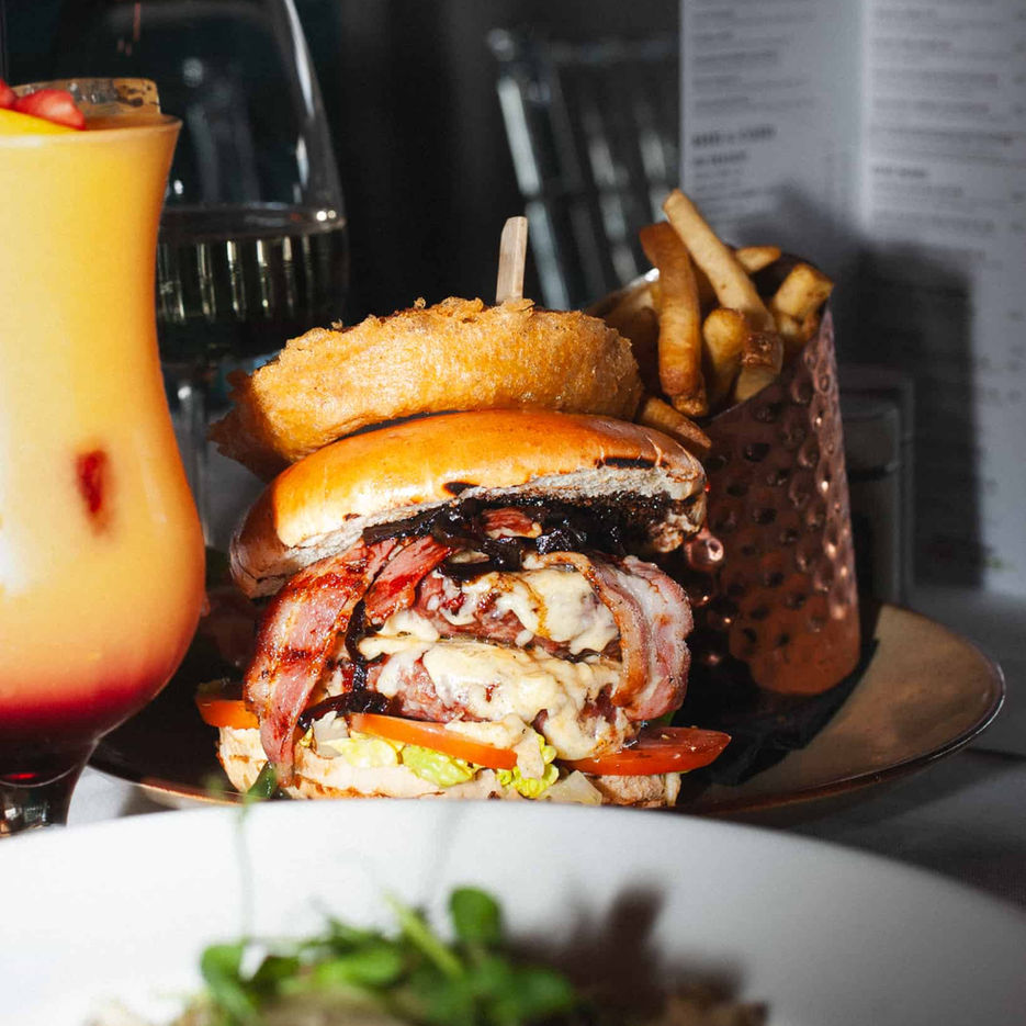 Casa's double cheese burger with bacon and an onion ring and fries, and a fruity cocktail