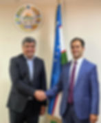 Two men shaking hands before Uzbekistan flag and emblem.