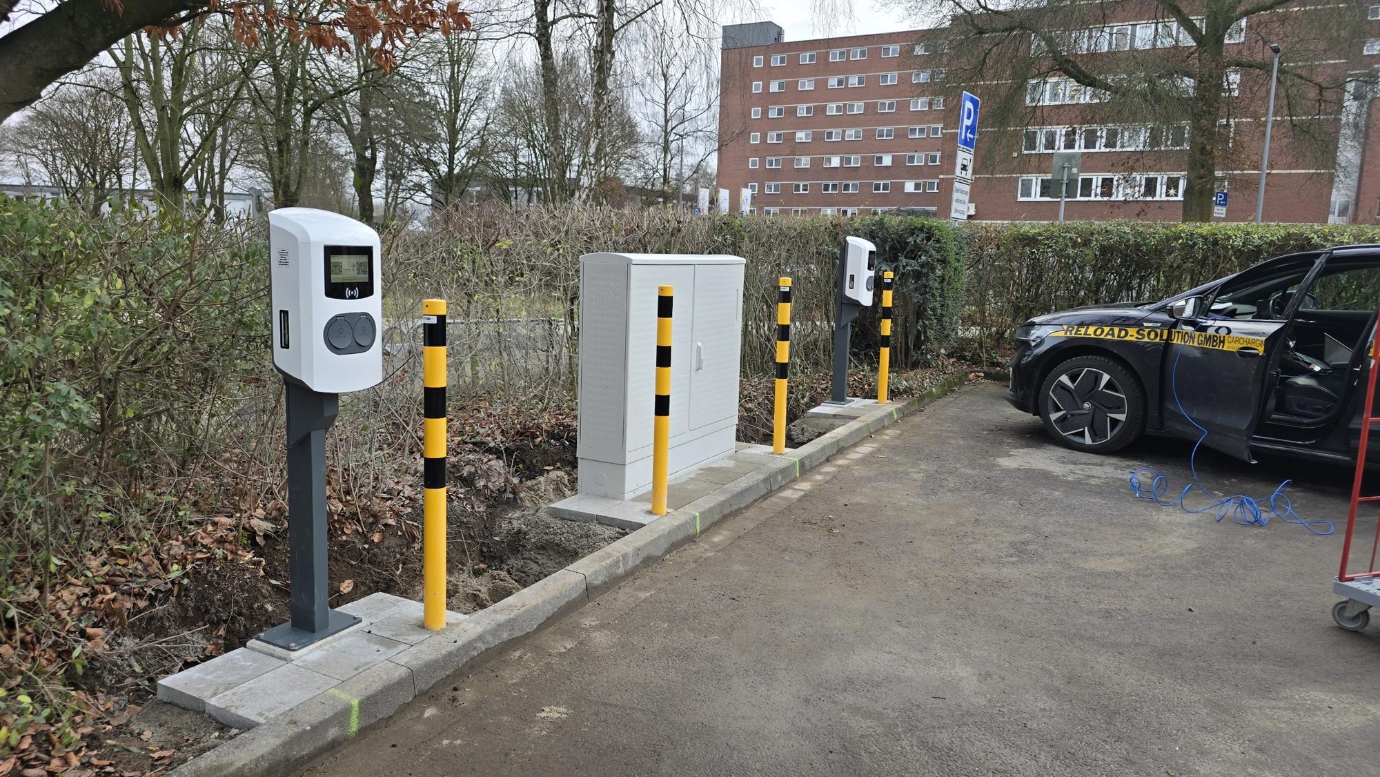 AC-Ladesäulen mit Verteilerschrank und Anfahrschutz, daneben ein Fahrzeug von Reload-Solution