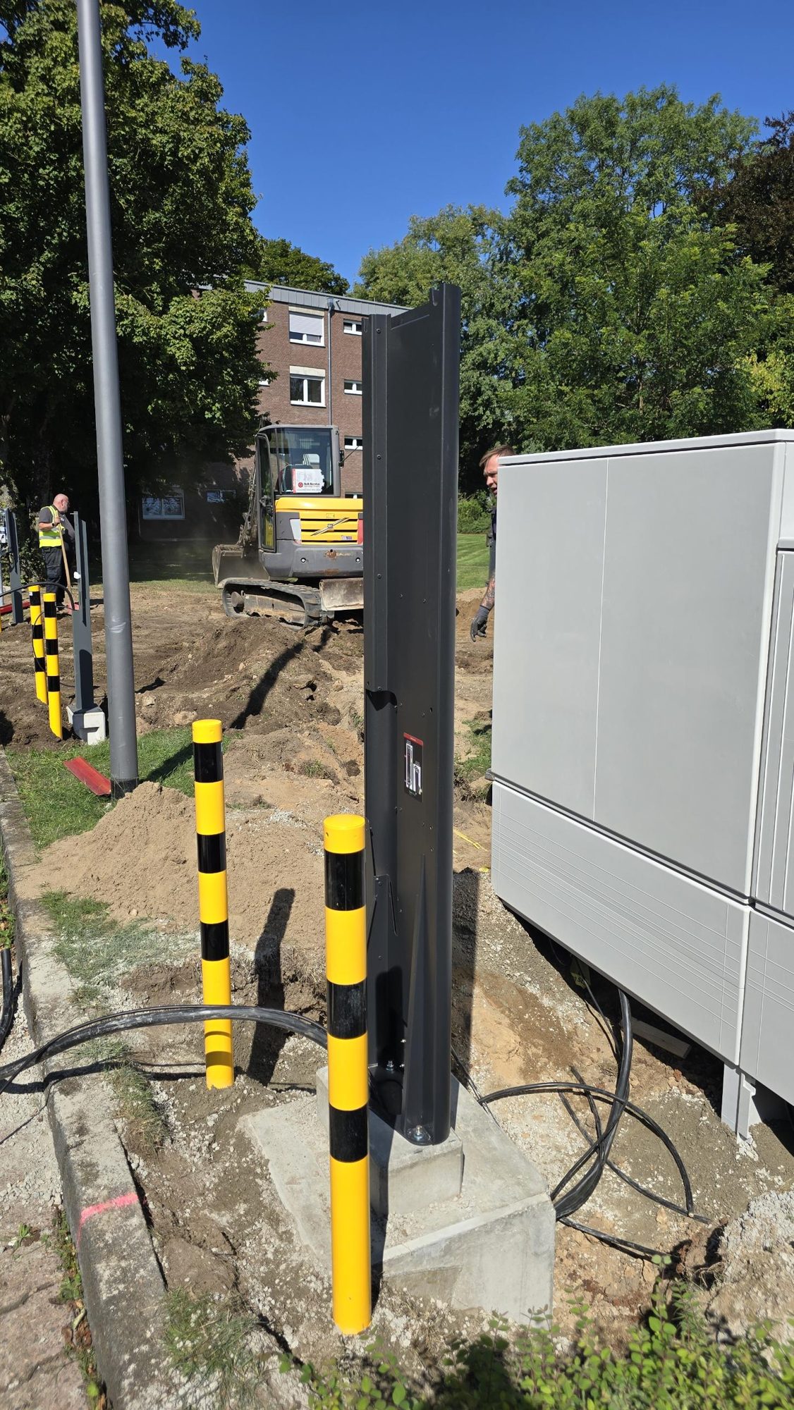 Baustelle mit Bagger, Ladesäulen-Stelen und Anfahrschutz