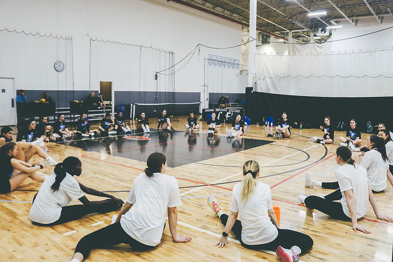 Grateful for Guidance: This photo depicts a post-camp gathering, with everyone seated on the floor, attentively listening to the coaches' feedback. It embodies a sense of unity, growth, and a shared passion for volleyball. The image showcases the importance of continuous learning, the strong bond between players and coaches, and the commitment to improvement that defines our team's journey.