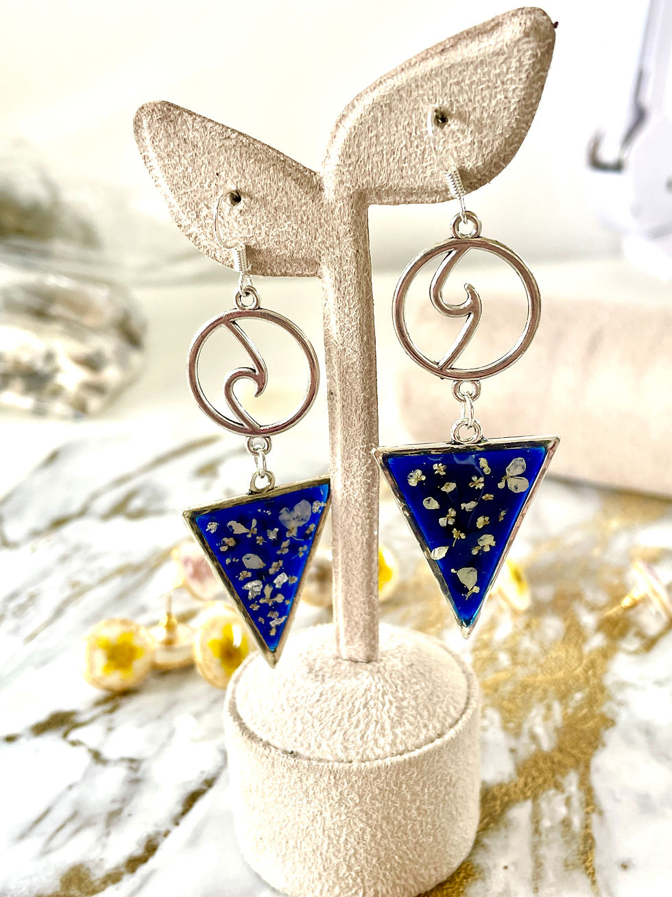 Thumbnail: Sterling silver blue  triangle pair of earrings made of UV Resin with dried white flowers, on the earrings stand