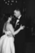 Bride and groom dance closely at a wedding, surrounded by onlookers. Dim lighting with string lights above. Elegant and intimate mood.