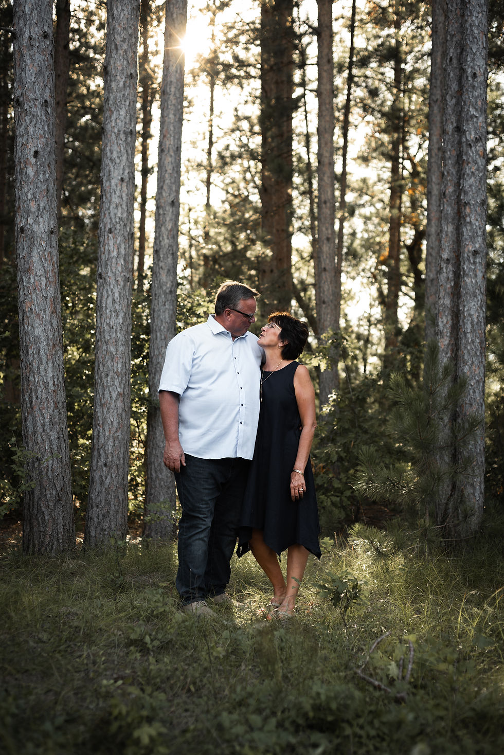 older man and woman embracing and looking at each other in front of tall pines with the sun shining through in Wisconsin Dells Wisconsin