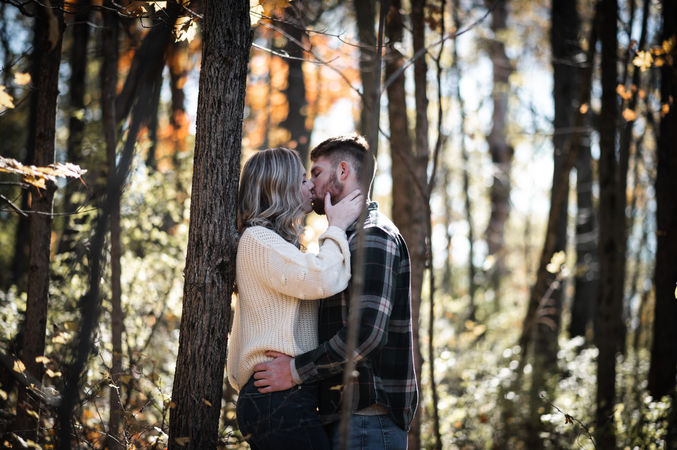 woman leaning on tree man leaning in and kissing her autumn colors in forest 