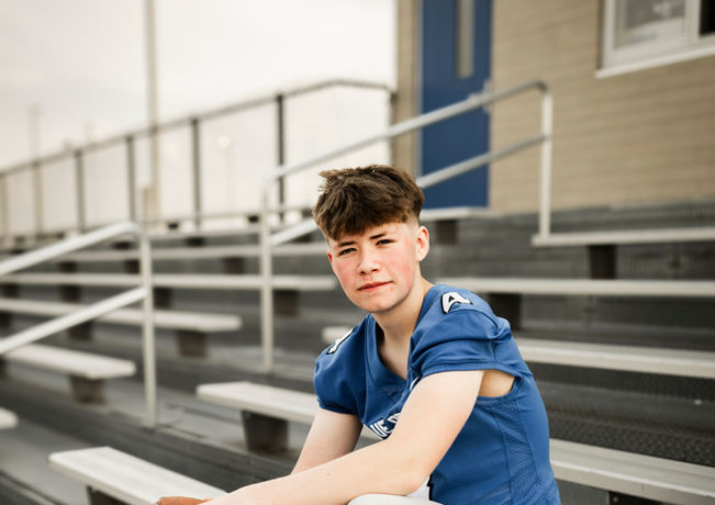 Senior boy with football jersey on sitting on bleachers holding a football in Lodi WI