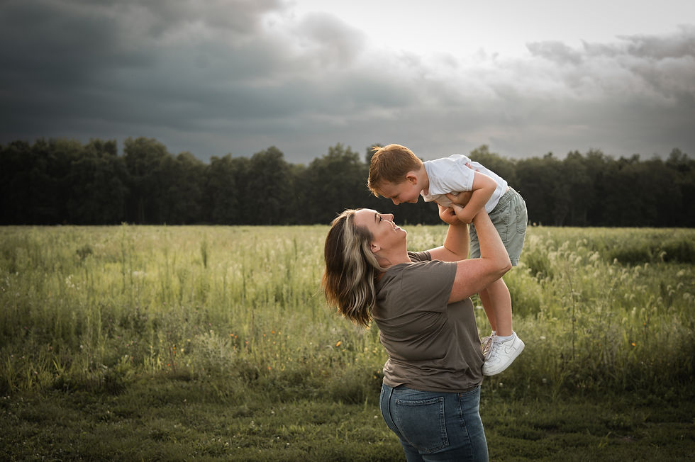 Woman holding small boy up in the air and smiling sunlit grass in background and cloudy storm clouds at Silverwood County Park in Edgerton Wisconsin