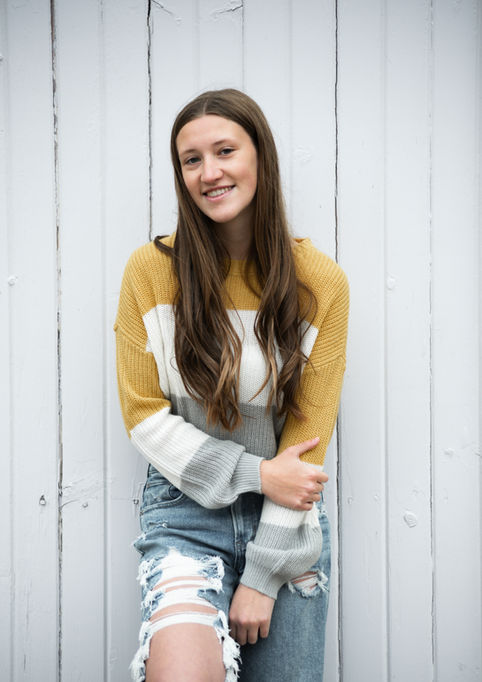 teenager with long brown hair and sweater leaning against white wall smiling downtown lodi wisconsin