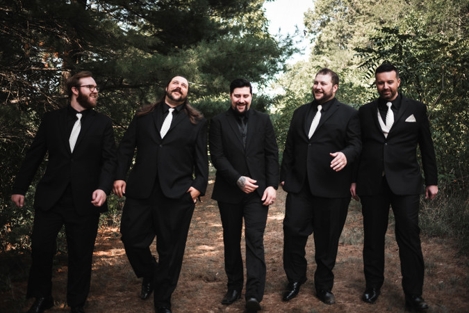 groomsmen and groom walking down wooded path and smiling at Whispering Pines Event Center in Poynette Wisconsin