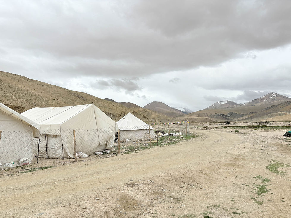 White tents beside a dirt road in a barren mountain valley under heavy gray clouds. AvVida.co.uk - Life is an Adventure / La Vida es Una Aventura