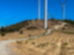 Wind turbines on a grassy hill under a clear blue sky. A winding dirt path leads to the turbines, with a small tree visible nearby. ⁨Bogas de Cima⁩, ⁨Beira Baixa⁩, ⁨Portugal⁩, Portugal ACT