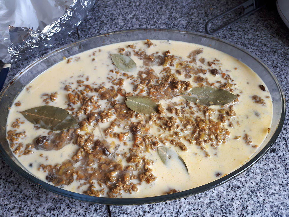 Bobotie in a glass dish on a granite countertop. The dish features minced meat, creamy sauce, bay leaves, and visible raisins. AvVida.co.uk Adventure Motorcycle Travel South America Buenos Aires, Argentina