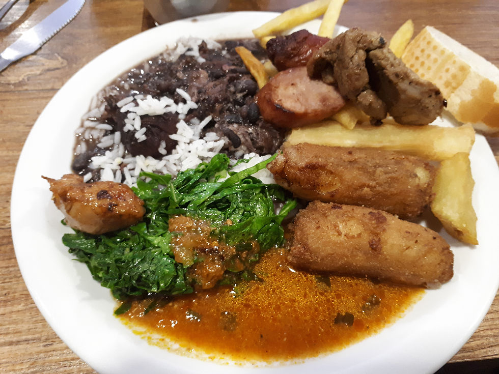 A plate of Brazilian feijoada with rice, beans, fries, greens, sausage, bread, and fried rolls on a wooden table, creating a hearty vibe. AvVida.co.uk - Adventure Motorcycle Travel South America