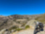 Motorcycle covered in stickers parked on a rocky mountain road under a clear blue sky. Rugged, scenic landscape creates a sense of adventure. Barragem do Covão do Ferro