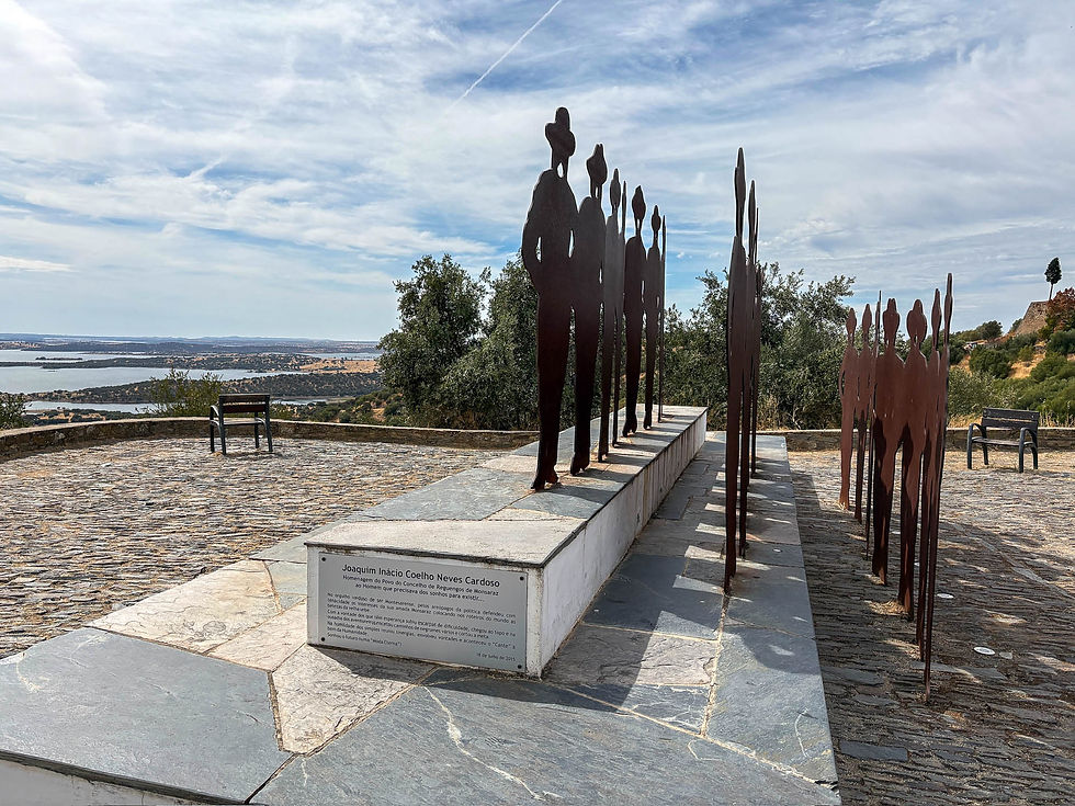 Silhouette sculptures on a stone platform overlooking a scenic landscape with a lake. Blue sky with light clouds; text plaque in front. AvVida.co.uk Adventure Motorcycle Travel with Turkana Gear
The memorial below Monseraz Castle in the car park