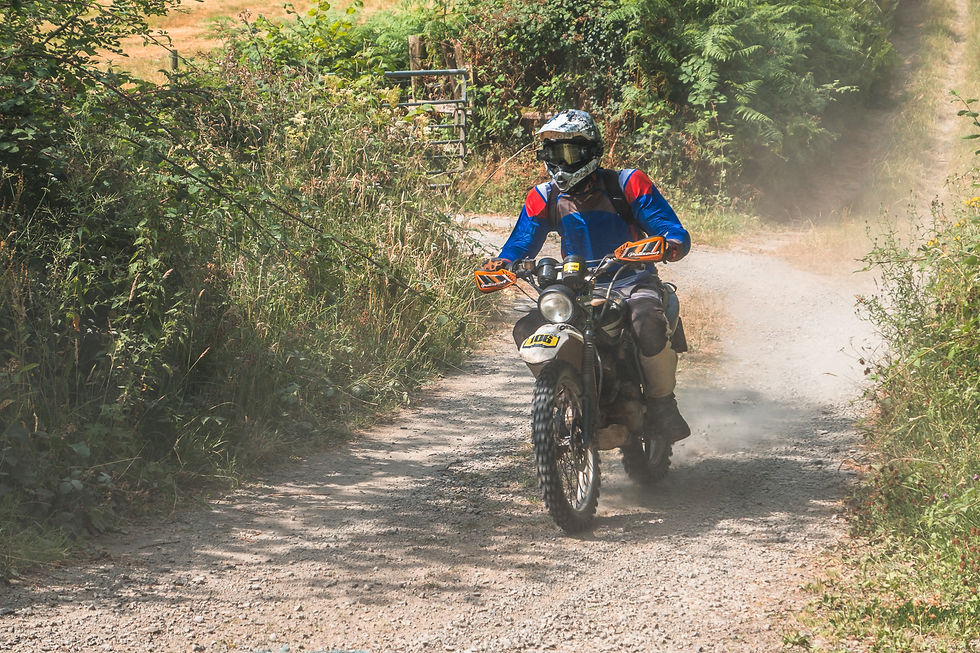 Scott `Lewis on his Lexmoto navigates a forest trail during the Beacons Rally 2026, surrounded by lush greenery and kicking up dust.