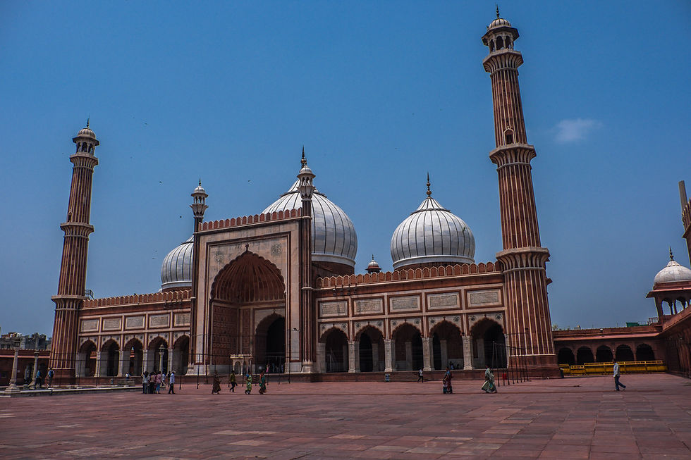 Grand mosque with white domes and tall minarets under a clear blue sky, with a few people walking across the courtyard. AvVida.co.uk - Life is an Adventure / La Vida es Una Aventura