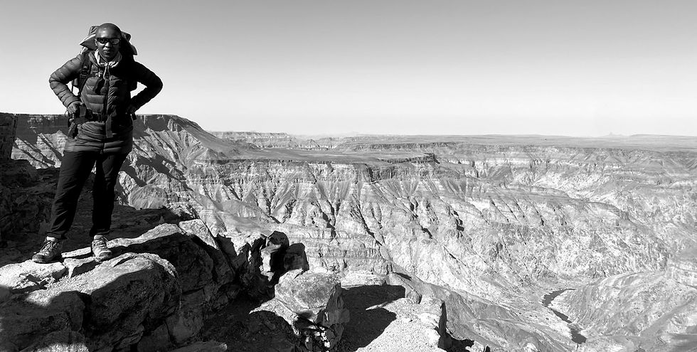 Dimpho Hlungwane stands confidently on the edge of a mountain. The expansive view highlights the intricate formations and vastness of the terrain, capturing a moment of exploration, courage and awe in nature's grandeur.