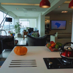 Foto Realista. Design de Interiores. Bancada da cozinha, área conjunta com a sala de estar. Janelas com iluminação natural indireta.