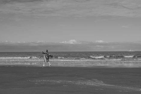 Speelse zwart wit foto op het strand van Cadzand met een vrouw die met armen, en sjaal, vrij over het strand dartelt.