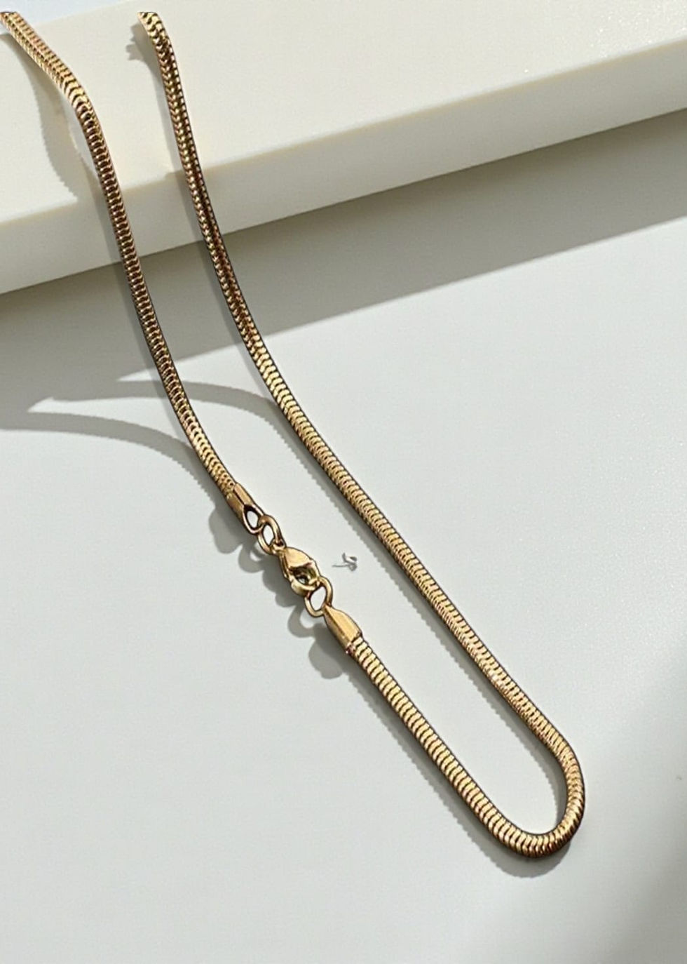 Close-up of a stylish Snake Bone Gold Chain on a white surface.