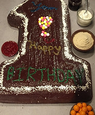 A chocolate cake shaped like the number 1, decorated with frosting and festive toppings, perfect for a first birthday celebra