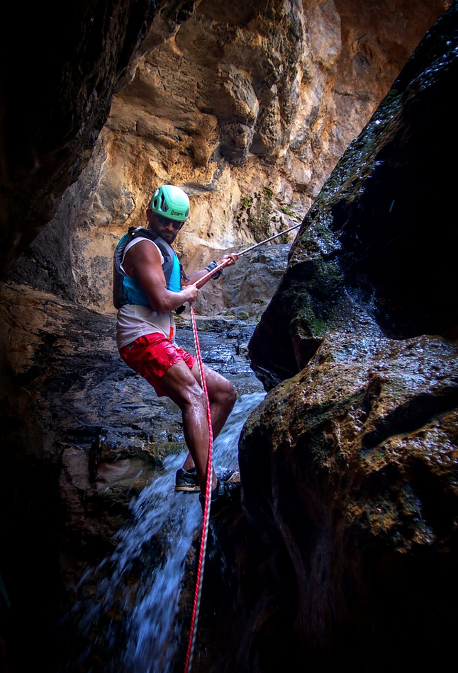 Adventurer using a rope beside a waterfall in Wadi Kamah, Oman