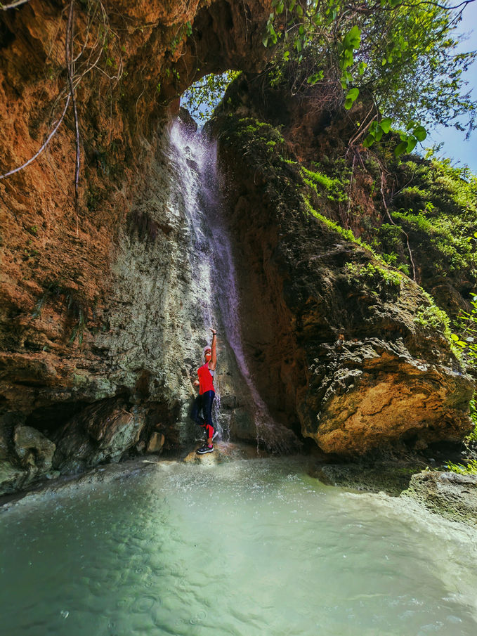 Traveler standing beneath a waterfall inside a hidden canyon in Dhofar