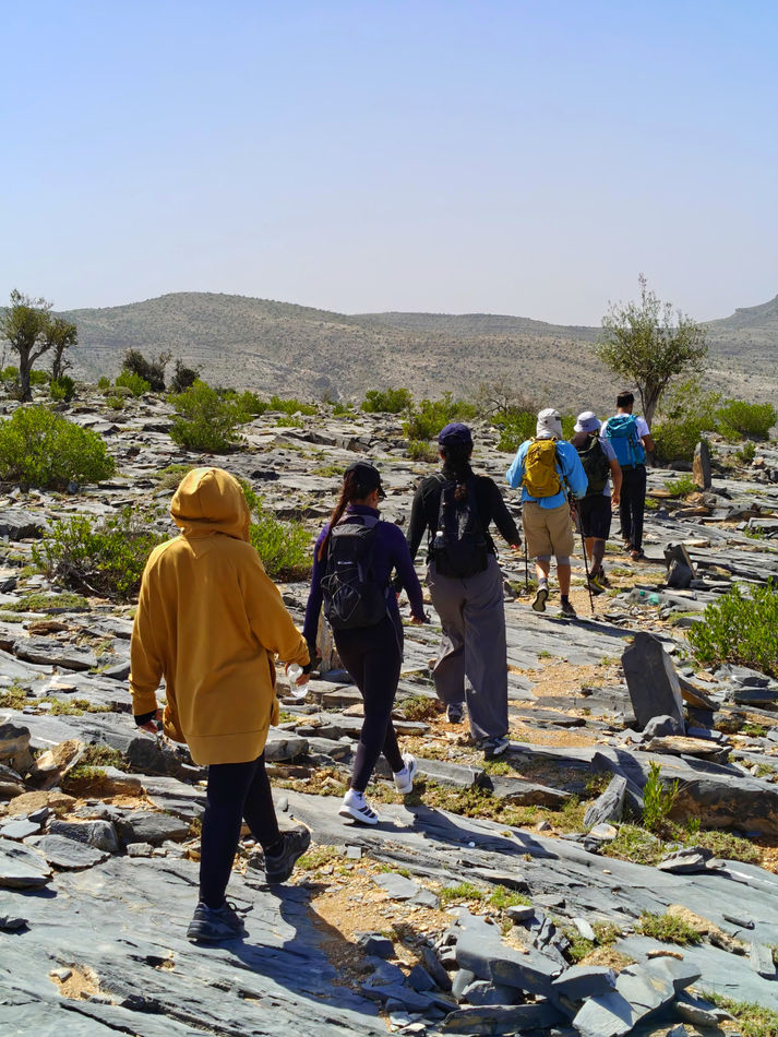 Hikers walking across a rocky mountain trail during the Wadi Bani Habib to Wadi Qasha adventure tour