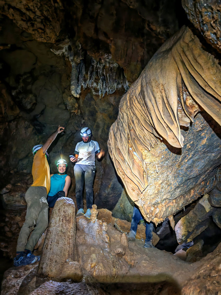 Visitors exploring a large cave chamber with rock formations inside Aamur Cave, Oman