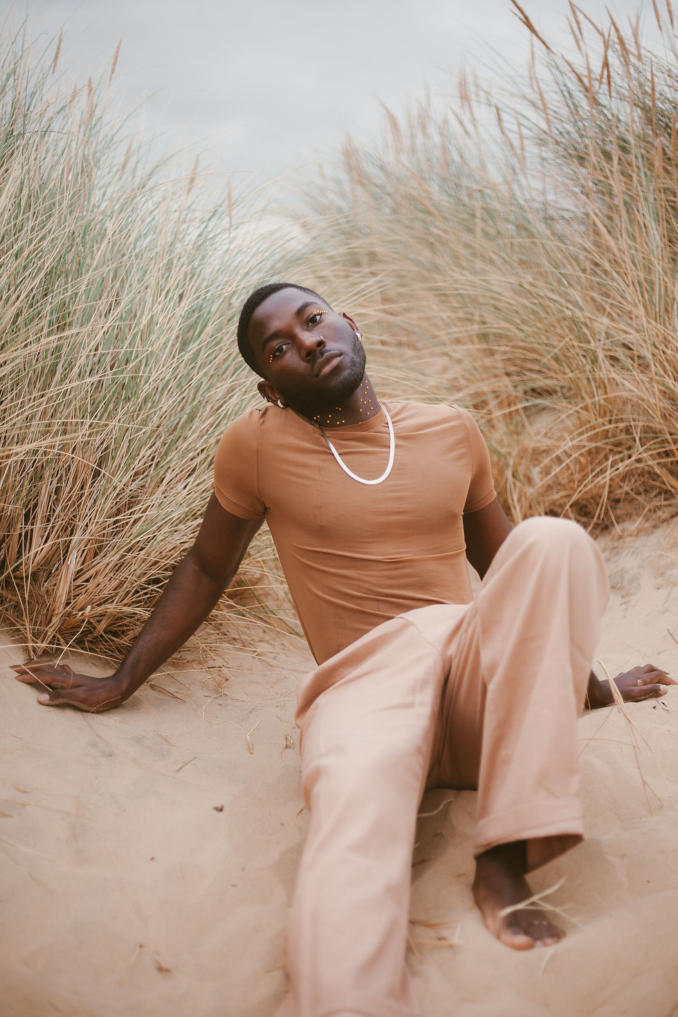 A man sitting on a sandy beach wearing brown clothes