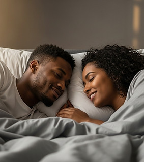 Smiling couple in bed, heads touching on soft pillows and sheets.