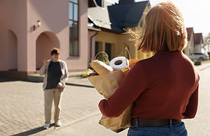 woman approaching older woman with cane holding a bag of groceries