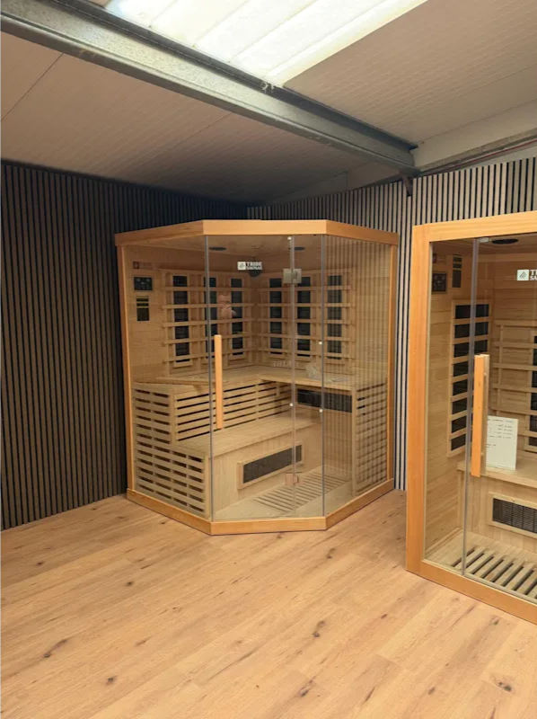 Modern sauna interior with wooden bench, rocks on a heater, and a digital thermostat displaying 21°C.