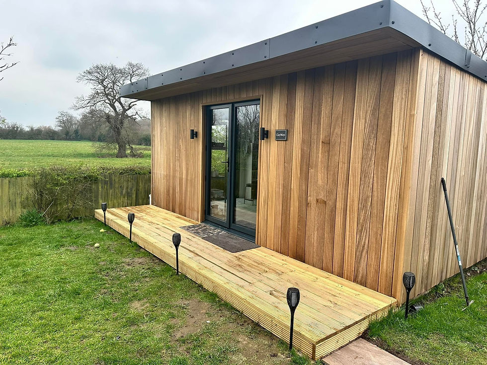 Modern timber-clad garden studio cabin featuring a wooden decking platform with outdoor solar lights and glass patio doors overlooking open fields