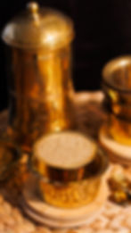 A 45-degree angle view of a brass tumbler and bowl filled with frothy South Indian filter coffee, with a traditional brass coffee filter placed in the background.