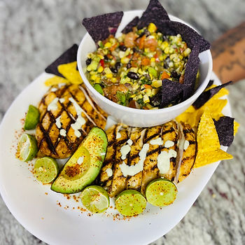 Plate of citrus grilled chicken strips with lime slices, served with a bowl of colorful black bean and corn salsa and blue corn tortilla chips.