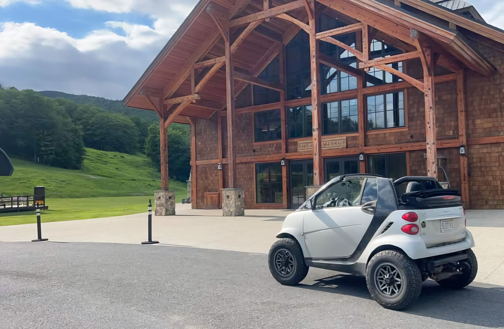 White Lifted smart car parked, large building in background, BRAAP Store Smart Car Lift Kits.